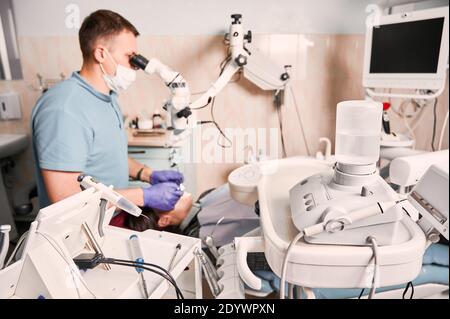 Close up of modern dental machine with stomatologist and patient on blurred background. Male dentist using microscope while checking woman teeth. Concept of dentistry and dental equipment. Stock Photo