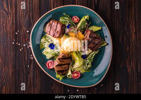 Eggs benedict with beef meat on a large white plate.. Traditional english breakfast with eggs Benedict, cherry tomato, lettuce. Benedict egg served on Stock Photo