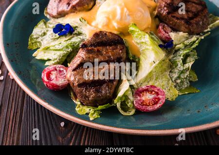Eggs benedict with beef meat on a large white plate.. Traditional english breakfast with eggs Benedict, cherry tomato, lettuce. Benedict egg served on Stock Photo