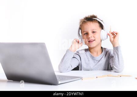 horizontal portrait of a blond caucasian boy using white headphones and a laptop looking at camera with white background Stock Photo