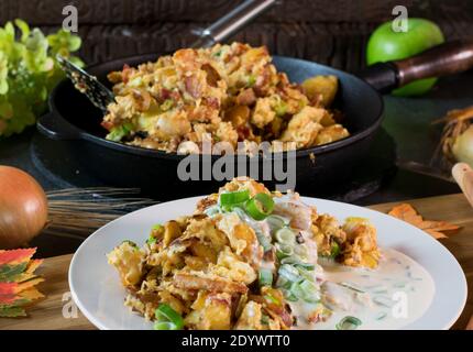 rustic meal with fried potatoes, eggs, bacon an heavy sour cream sauce served on a plate. Iron pan is to be seen in the background Stock Photo