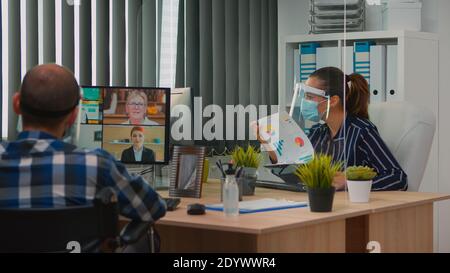 Immobilized freelancer with protection mask in wheelchair having videomeeting during a coronavirus pandemic in new normal business office. Freelancer working in company respecting social distance. Stock Photo