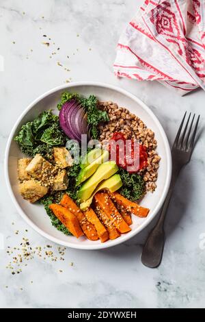 Baked vegetables, avocado, tofu and buckwheat buddha bowl. Vegan lunch salad with kale, baked sweet potato, tofu, buckwheat and avocado in a white bow Stock Photo