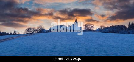 village with a church on a hill at sunset in winter, beautiful sky with illuminated clouds, Vezovata Plane, Czech republic Stock Photo