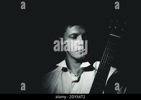 Young man with classic guitar. Black and white dramatic portrait, low key. Stock Photo