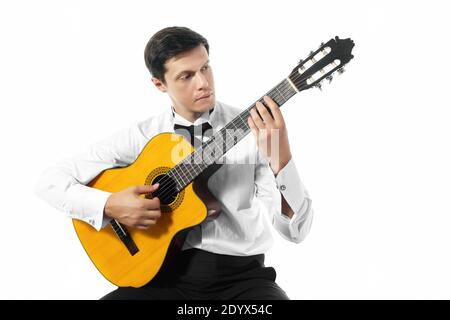 Young man in white shirt with bow tie posing with classical guitar in studio on white background. Stock Photo