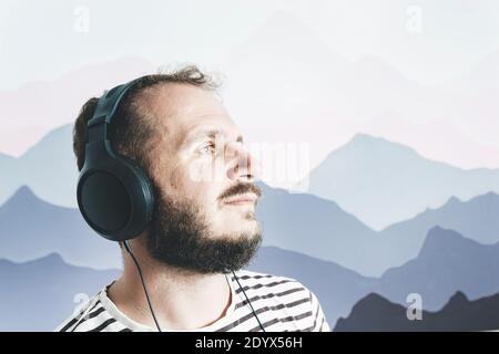 Bearded happy man in a striped T-shirt listens to music with big headphones. looks away. Stock Photo