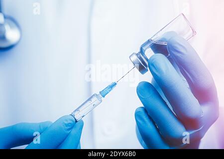 Close up doctor arm using syringe and ampoule, white robe dressed doctor on blurred background. Medical, immunization and vaccination concept. Stock Photo
