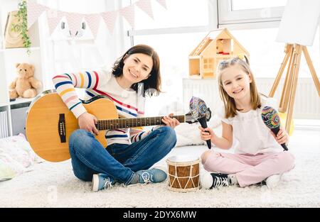 Nice little girl and mother playing musical instruments in kids room Stock Photo
