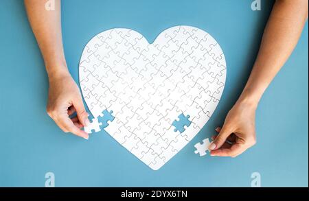 White puzzle in heart shape. Hands with white details of puzzle on blue background. Stock Photo
