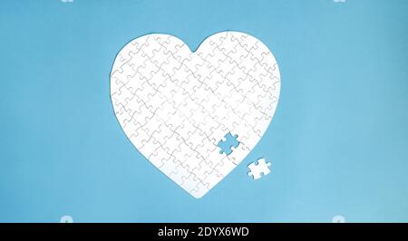 White puzzle in heart shape. White details of puzzle on blue background. Stock Photo