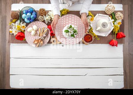 Table setting for the Easter holiday. Tea, homemade cake, eggs and flowers on a wooden table. Stock Photo