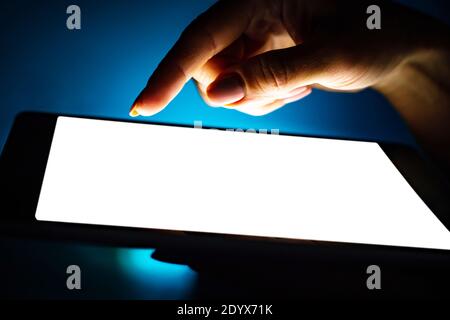Close up view of girl using tablet with white screen on dark background Stock Photo