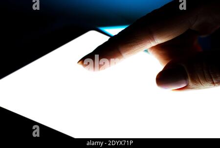 Close up view of girl using tablet with white screen on dark background Stock Photo