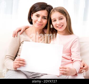 Mother and daughter holding empty blank sheet of paper A4 in hands at home Stock Photo