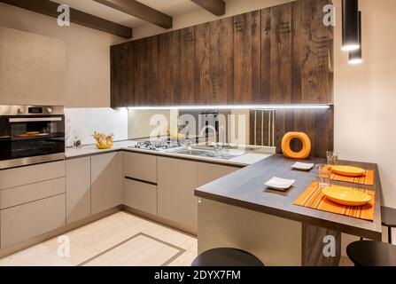 Interior of modern fitted kitchen with orange accents and neutral beige coloured cabinets with recessed lighting Stock Photo