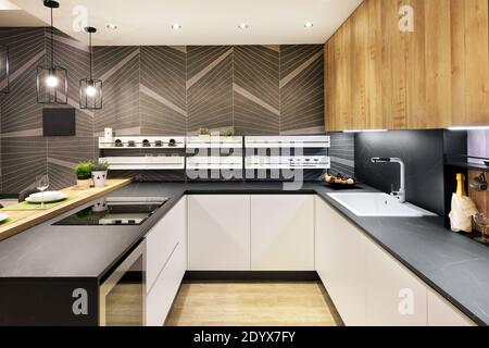 Long narrow fitted kitchen interior with built-in appliances and white fronted cabinets lit by ceiling lights in a receding view Stock Photo
