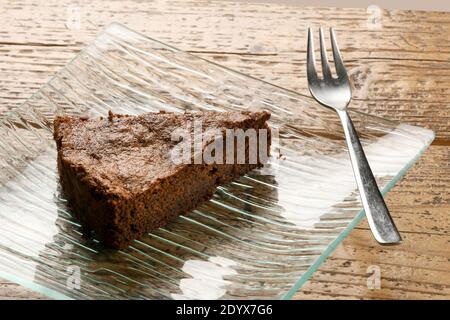 Single slice of freshly baked chocolate cake served on a stylish rectangular glass dish with fork on a wooden table in a high angle view Stock Photo