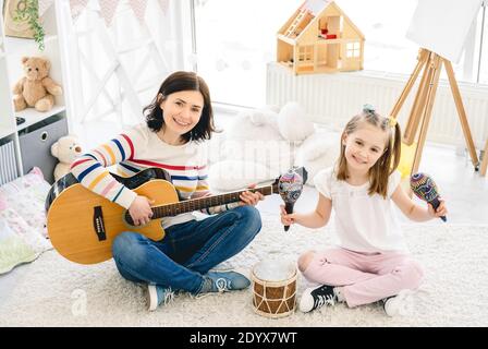 Nice little girl and mother playing musical instruments in kids room Stock Photo