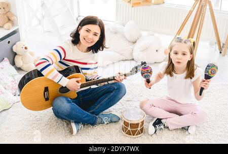 Beautiful woman playing guitar and singing with cute little girl Stock Photo