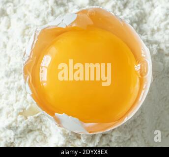 White egg and egg yolk on flour background, close up Stock Photo