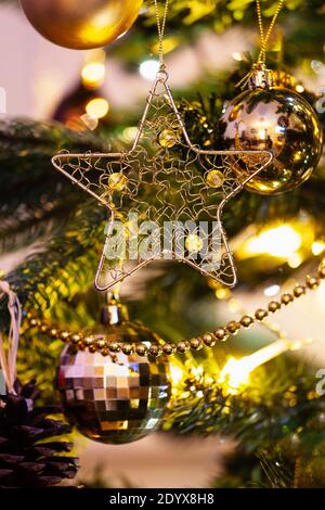 Golden Christmas star hanging on a Christmas tree, with lights and bauble decorations hanging in the background. Stock Photo