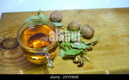 Photo of herbal and linden tea inside the glass pot together with linden tea leaves and broken and not broken walnuts on the wood table. Stock Photo