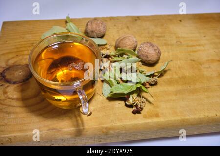 Photo of herbal and linden tea inside the glass pot together with linden tea leaves and broken and not broken walnuts on the wood table. Stock Photo