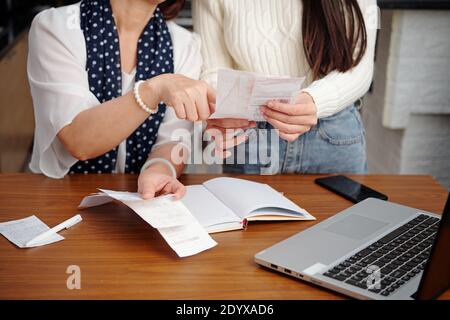 Hands of senior woman explaining adult daughter how to pay utility bills online via website on laptop Stock Photo