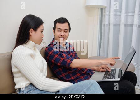Young Asian couple filling forms and documentd online on laptop when sitting on couch in living room Stock Photo