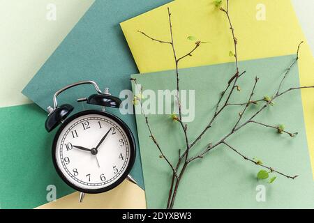 Black alarm clock and branches of tree with young blossoming leaves on geometric green shades background. Top view Flat lay Template for your text, de Stock Photo