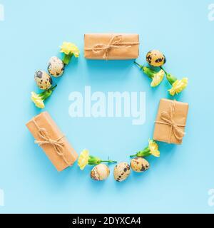 Happy easter festive circle frame. Easter layout made of quail eggs, yellow flowers and craft gift on blue background with copy space Creative Flat la Stock Photo