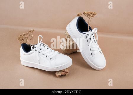 Ethical vegan shoes concept. A pair of white sneakers with dry flowers on the stones against a background of neutral beige craft paper. Stock Photo