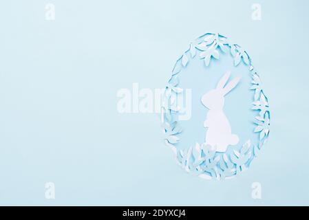 Easter egg made of paper leaves with white bunny on blue background. Cut from paper. copy space Stock Photo