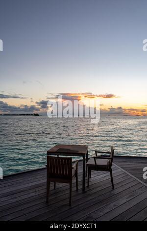 Wodden dining table on a terrace overlooking the sea, with sunset in the background, Maldives. Stock Photo