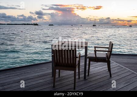 Wodden dining table on a terrace overlooking the sea, with sunset in the background, Maldives. Stock Photo