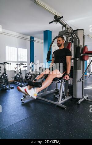 Handsome man doing leg exercises in a gym. Focus on him. Vertical Stock Photo