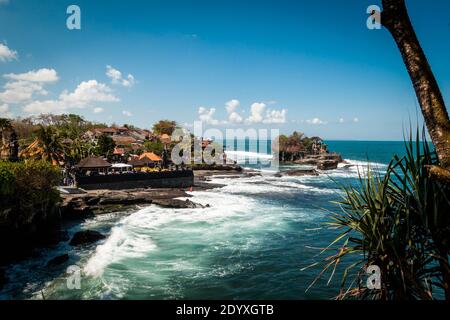 A long distance view of Tanah Lot Temple in the wavy sea on a sunny day in Bali Stock Photo