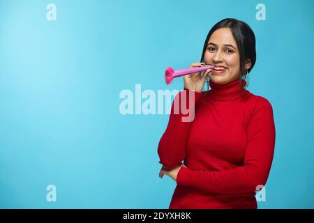 Young Female blowing party horn wearing red sweatshirt celebrating new years Stock Photo