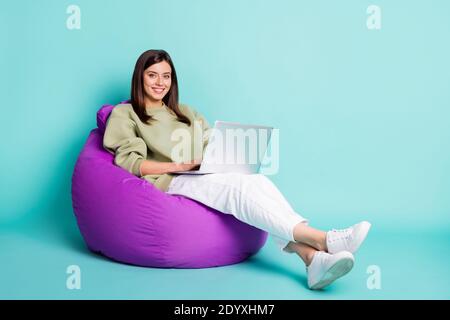 Photo portrait full body view of girl working on laptop sitting in purple beanbag armchair isolated on vivid teal colored background Stock Photo