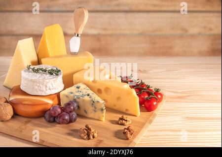 composition different types of cheese with walnuts, tomato and grapes on rustic wooden background. Assortment of different cheese. copy space Stock Photo