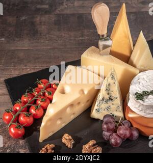 various types of cheese on rustic wooden table. Cheese plate: Parmesan, cheddar, gouda, camembert, brie with nuts on wooden board on dark background w Stock Photo