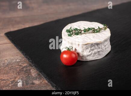 Delicious brie cheese on black background. Brie type of cheese. Camembert. Fresh Brie cheese and a slice on stone board. Italian, French cheese. Stock Photo