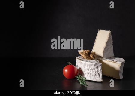 brie cheese with tomato and walnut on black background. Brie type of cheese. Camembert. Fresh Brie cheese and a slice on stone board. Italian, French Stock Photo
