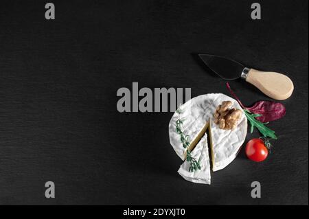 Delicious brie cheese with tomato and walnut on black background. Brie type of cheese. Camembert. Fresh Brie cheese and a slice on stone board. Italia Stock Photo