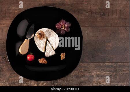 Delicious brie cheese on black plate. wooden rustic table. Brie type of cheese. Camembert. Fresh Brie cheese and a slice with knife. Italian, French c Stock Photo