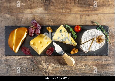 cheese plate. different cheeses laid out on long black stone Board. blue cheese Dorblu, smoked Suluguni, brie, Maasdam, cheddar, Parmesan with walnuts Stock Photo