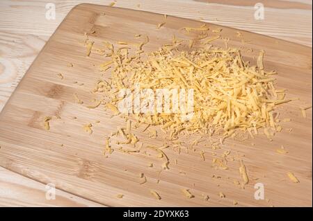 grated cheese on a wooden cutting Board. Grated cheese on the table. Pile of grated cheddar cheese Stock Photo
