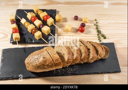 sliced bread and snacks on a skewer. canapes from olives, cheese and cherry tomato on skewers on black board. finger food. Stock Photo