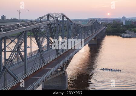 Ottawa, Canada - July 24 2014: A sunset view of Alexandra Bridge which links Ottawa, Ontario to Hull, Quebec. A crew of rowers passes under the bridge Stock Photo